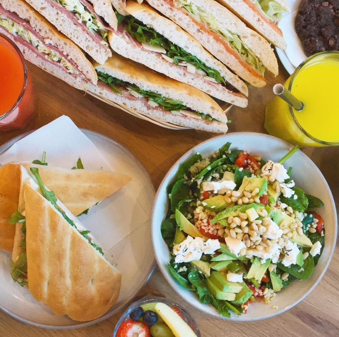 Panini's met rucola en ham, een salade met avocado en feta en vers sap op tafel